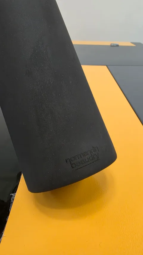 Custom engraved black ceramic carafe with precise Normandin Beaudry logo on yellow workshop workbench.