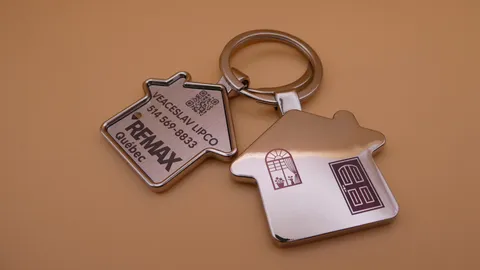 Custom house-shaped metal keychains with laser-engraved RE/MAX branding, QR codes, and color marking. A personalized gift for real estate agents created by TechArt Concept.